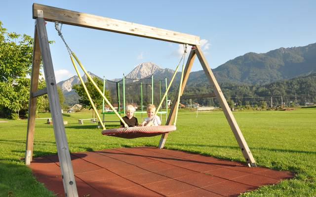 Zwei Kinder auf der Schwingschaukel im Hintergrund Berglandschaft