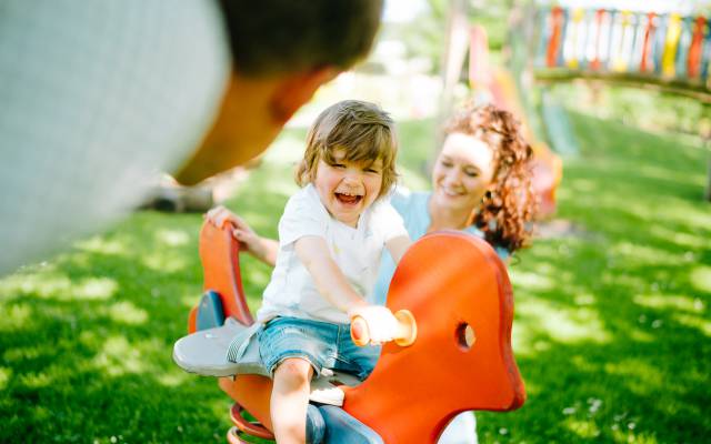Familie hat Spaß auf dem Spielplatz - Kind Wippt auf Holzpferd