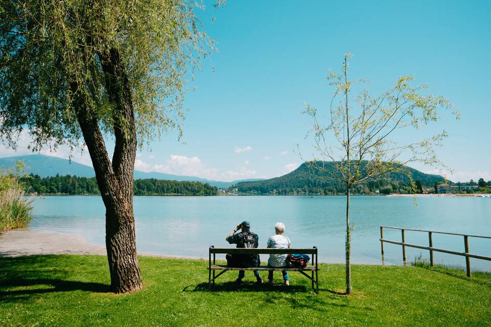 Paar sitzt auf einer Bank am Faaker See und genießt die Aussicht